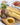 Pasta on a wooden board with olive oil, capers, and red peppers.