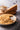 Plate of mushroom risotto with a wedge of Parmesan cheese and a bowl of mushrooms on a wooden table with a brick background