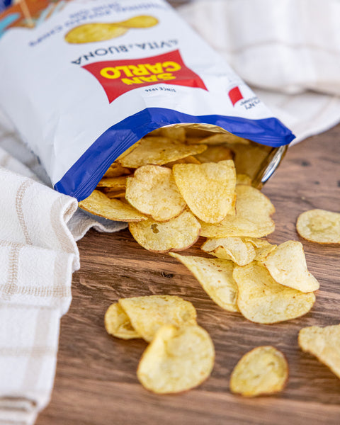 Open bag of San Carlo brand potato chips on a wooden surface with some chips spilling out.