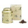 A gold-colored metal tea caddy labeled 'Gabrielle' from La Via del Tè, with a matching box and loose leaf tea visible in front.