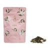 Pink tea packaging with floral designs and green tea leaves on a white background