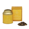 A gold aluminum tin of Sogno di Michelangelo loose leaf tea with its packaging box and a small pile of dried tea leaves and petals in front of it.