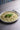 Pesto risotto in a white bowl on a wooden table with a fork.