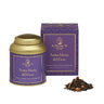 A gold-colored La Via del Té Santa Maria del Fiore loose leaf tea tin with a purple label, accompanied by a purple box with gold text. A small pile of dry tea leaves and flowers is displayed in front.