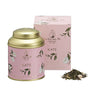 A La Via del Té branded tea tin labeled 'Kate' with a pink background and green leaves, accompanied by a pink box, alongside a scattered pile of green tea leaves.